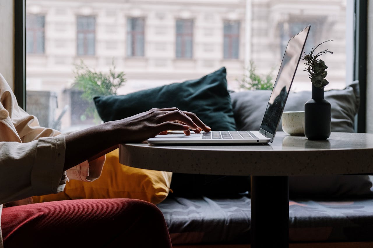 Close-up of a person typing on a laptop at a cozy cafe table with cushions.